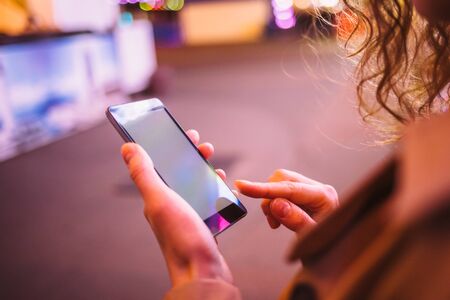 Young woman using smart phone pointing on screen on city street at night, close-up.の写真素材
