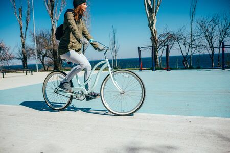 Young woman riding bicycle on sports field near sea on sunny spring day.の写真素材