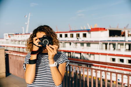 Young woman holding camera close to her face photographing city on sunny summer day.の写真素材