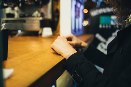 Young woman waiting for her order by putting her hands on wooden counter of street stall at night.の写真素材