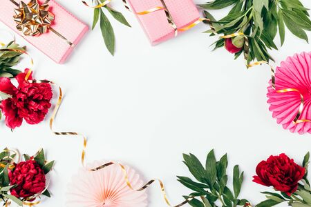 Festive floral flat lay frame of pink peony flowers, gift boxes with golden bows, ribbons and decorations on white background.の写真素材