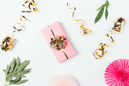 Festive flat lay composition of pink gift box with golden bow next to ribbons and decorations on white table.の写真素材