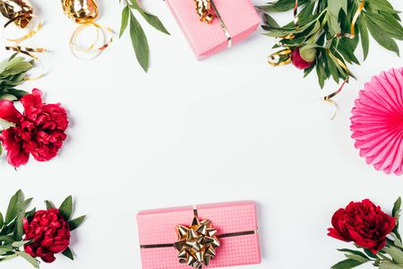 Festive flat layout of pink gift boxes next to fresh peony flowers and golden ribbons on white background.の写真素材