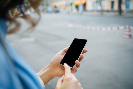 Unrecognizable young woman using mobile phone with blank display standing on city street during the...