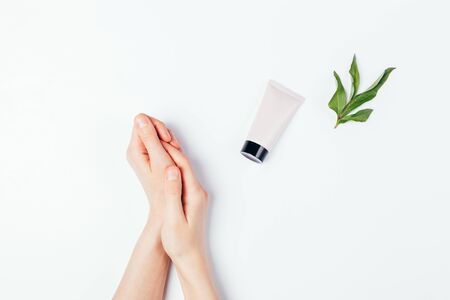 Soft female hands next to tube of skin care cream and fresh green leaf on white background, flat lay.の写真素材