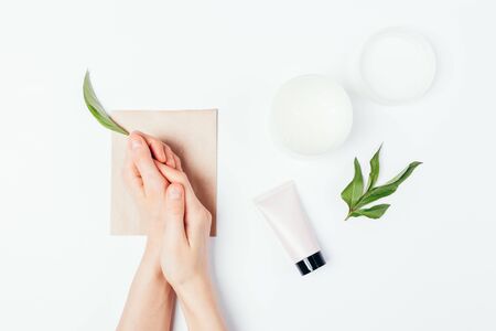 Tender soft female hands next to natural skin care cosmetic creams and green leaf on white background.の写真素材