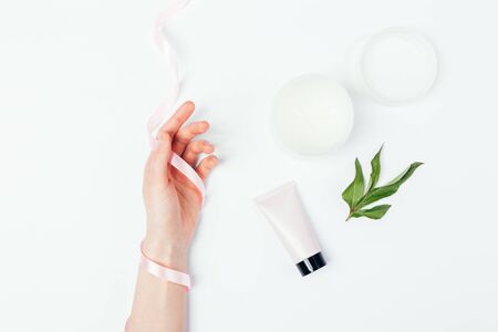 Natural skincare products cosmetic creams next to female's hand wrapped with silk ribbon on white background.の写真素材