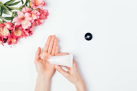 Female hands apply cosmetic skin care cream next to bouquet of fresh flowers on white background, flat lay.の写真素材
