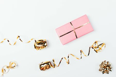 Pink gift box next to golden bow and ribbons on white background, flat lay.の写真素材