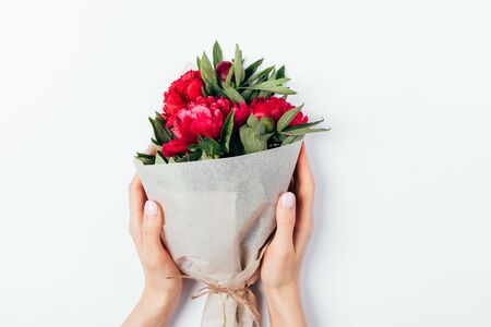 Female hands holding bouquet of peony flowers packed in brown eco paper on white table, top view.の写真素材