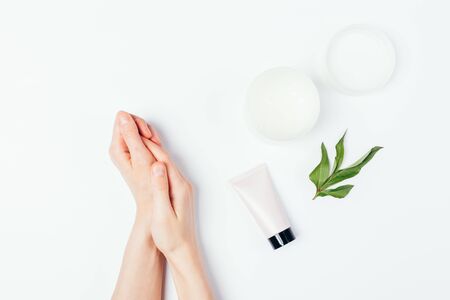 Soft female hands next to organic skin care cosmetic creams and green leaf on white background, top view.の写真素材