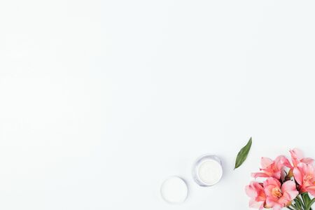 Flat lay composition beauty product moisturizer cream in open jar next to fresh pink flowers on white background with copy space.の写真素材