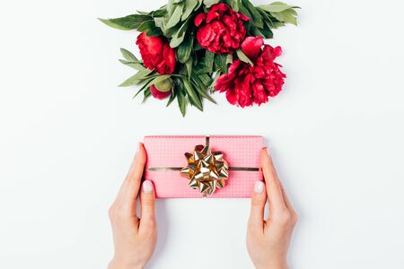 Floral flat lay composition of bouquet of pink peonies and gift box in female hands on white background.の写真素材