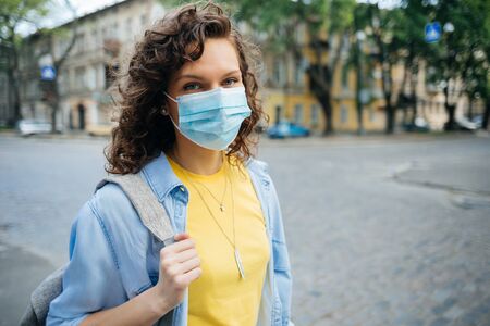 Young woman wearing medical mask for protection against the virus stands on european city street looking at camera.の写真素材