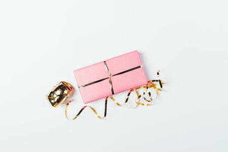 Unfinished pink wrapped gift box next to golden ribbon on white background, minimal flat lay arrangement.の写真素材