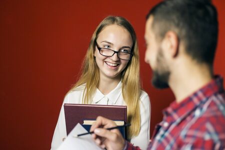 Two teenager students have a friendly study discussion holding books on red backgroundの写真素材