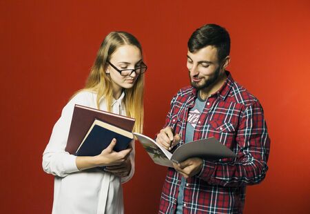 Two teenager students have a friendly study discussion holding books on red backgroundの写真素材