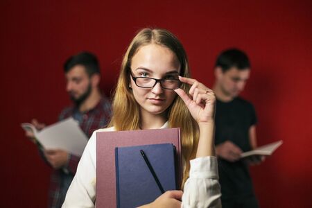 attractive happy smiling student blonde girl in white shirt with books on red background, student conceptの写真素材