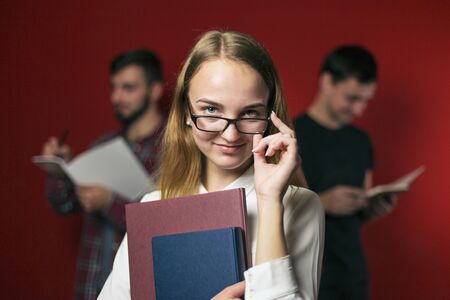 attractive happy smiling student blonde girl in white shirt with books on red background, student conceptの写真素材