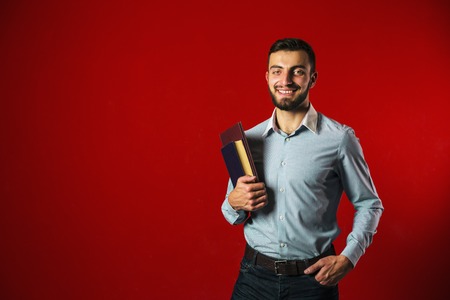 A portrait shot of a attractive handsome smiling student beard man with books on red background