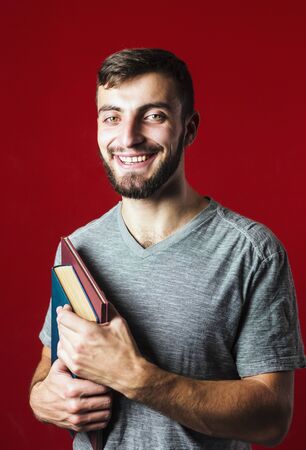 A portrait shot of a attractive handsome smiling student beard man with books on red backgroundの写真素材