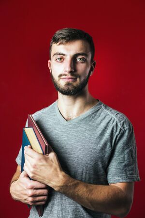 A portrait shot of a attractive handsome smiling student beard man with books on red backgroundの写真素材