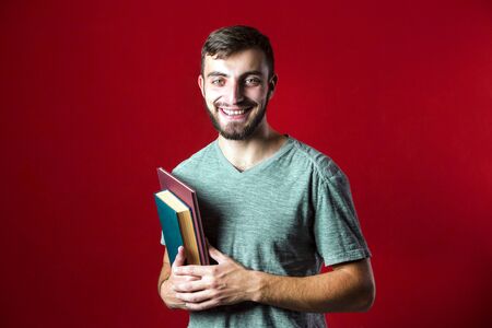 A portrait shot of a attractive handsome smiling student beard man with books on red backgroundの写真素材