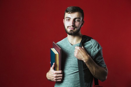 A portrait shot of a attractive handsome smiling student beard man with books on red backgroundの写真素材
