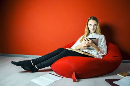 Young student girl studying sitting on the bag-chair near books and tablet pcの写真素材