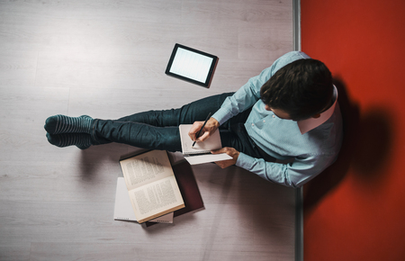 Young student man studying sitting on the floor near books and tablet pcの写真素材