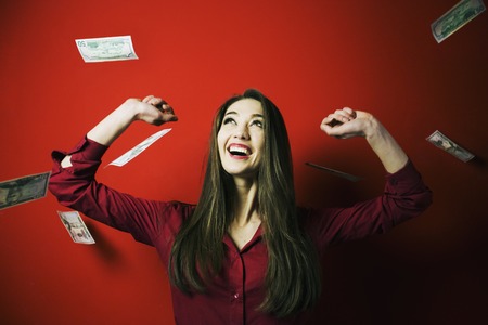 Attractive brunette woman with falling dollars banknotes red background, jackpot conceptの写真素材