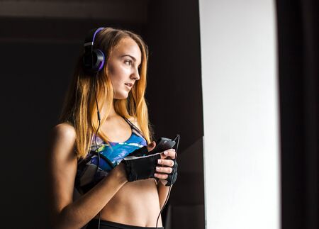 Attractive blonde girl in purple headphones with bottle in hand listening musci near the windowの写真素材