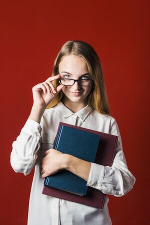 attractive happy smiling student blonde girl in white shirt with books on red background, student conceptの写真素材