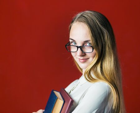attractive happy smiling student blonde girl in white shirt with books on red background, student conceptの写真素材