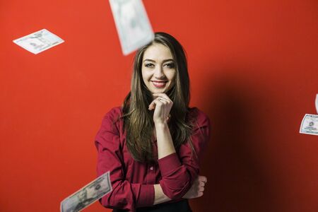 Attractive brunette woman with falling dollars banknotes red background, jackpot conceptの写真素材