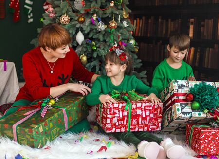 Mother with her happy kids have got gift boxes under Christmas treeの写真素材