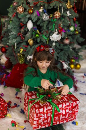 Kid girl holding surprize gift box before christmas treeの写真素材