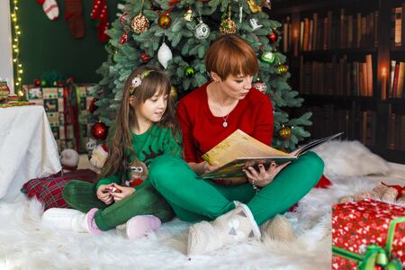 Mother with her daughter reading the book near dressed up christmas treeの写真素材
