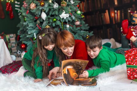 Mother with her kids reading the book near dressed up christmas treeの写真素材