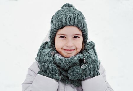 Portrait of a smiling kid girl wearing in grey hat and scarf outdoor in winter timeの写真素材