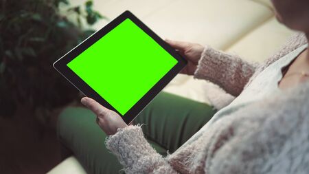 Indoor shot of a woman using tablet pc with green screen sitting on white sofa, horizontal orientationの写真素材