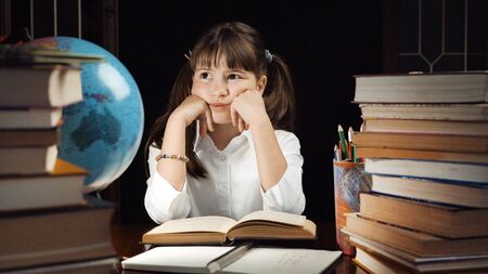 Eight years thoughtful school girl studying process, table place with books and globe, education conceptの写真素材