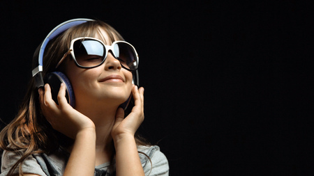 Studio shot of cute teenager girl wears headphones and sunglasses before black background, listening rhytmical music, youth freedom conceptの写真素材