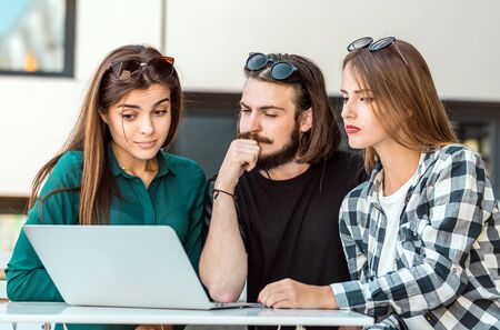 Group of students wear glasses have work conversation outdoor cafe, table with tablet computer before modern building wall, sunny dayの写真素材