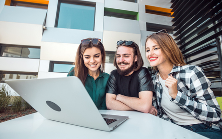 Group of students wear glasses have work conversation outdoor cafe, table with tablet computer before modern building wall, sunny dayの写真素材