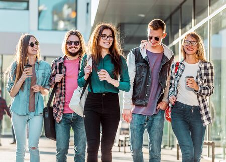 Group of student friends walking with cups of coffee having pleasant talk, sunsetの写真素材