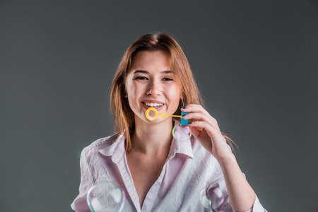 Beautiful girl having fun playing with soap bubbles on isolated studio gray backgroundの写真素材