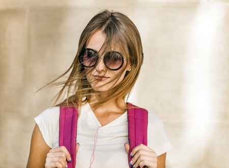 Beautiful caucasian fair hair student tourist girl in stylish sunglasses and with a pink backpack is...