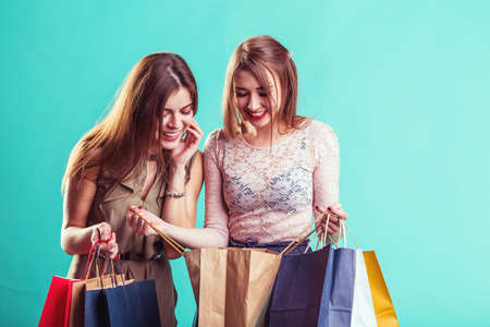 Friends girls smiling holding colorful shopping bags before blue indoor background, shopaholic conceptの写真素材