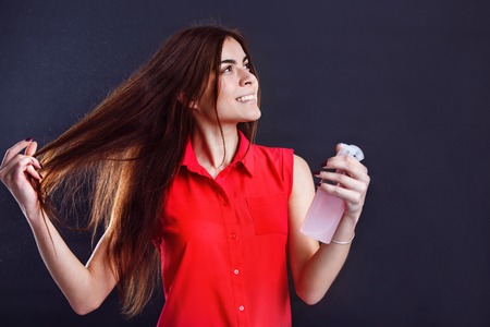 Cheerful brunette girl holds spray bottle on dark isolated backgroundの写真素材